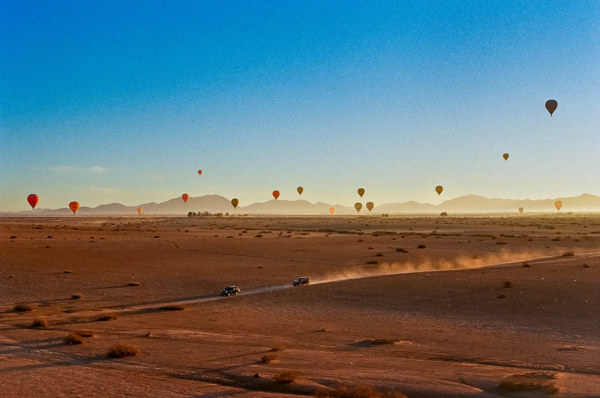 Montgolfières dans le ciel et véhicules sur les pistes d’Agafay au lever du soleil